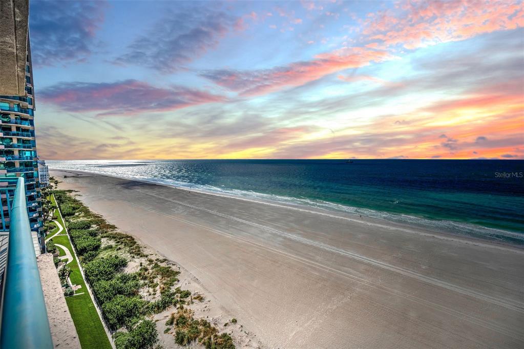 An elevated view from a balcony overlooking a sandy beach and the ocean at sunset — 1520 GULF BOULEVARD UNIT 1101, CLEARWATER BEACH, FL