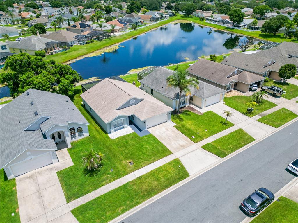 An aerial view shows suburban houses with driveways and backyards bordering a large pond — 3245 WHOOPING CRANE RUN, KISSIMMEE, FL