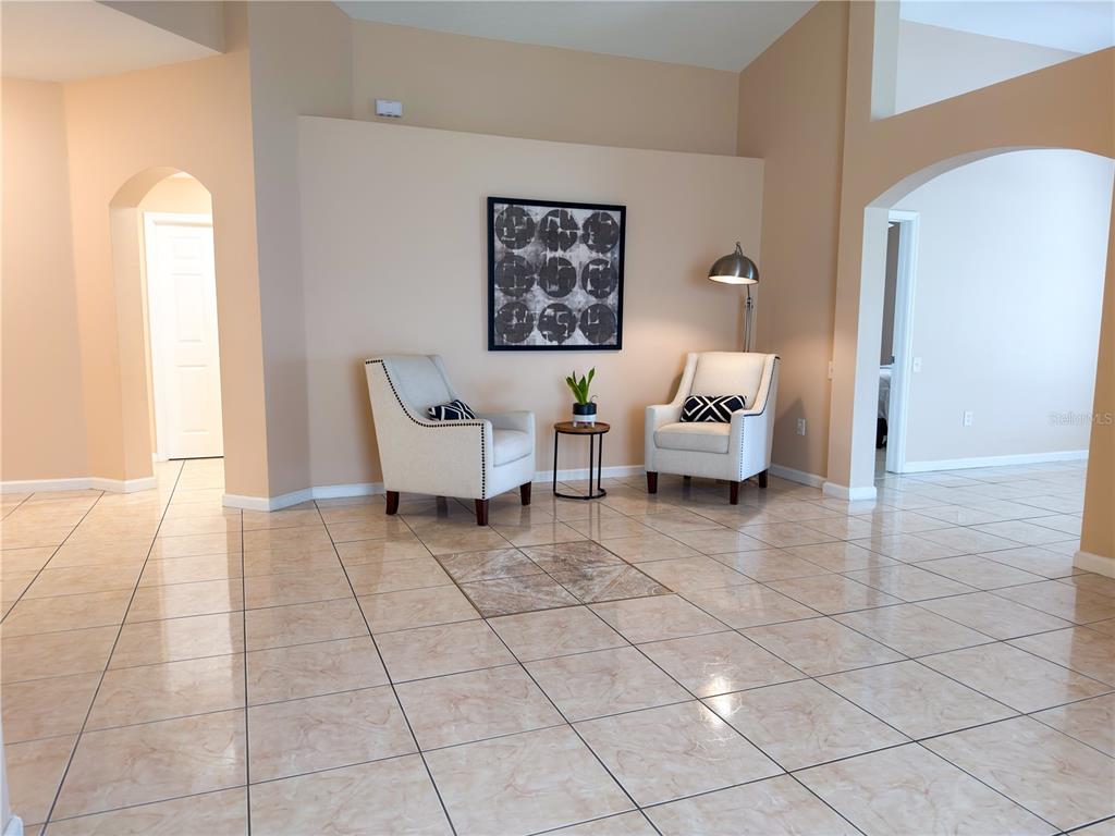 A living area features light-colored tile flooring, two armchairs, a small side table, and artwork — 3245 WHOOPING CRANE RUN, KISSIMMEE, FL