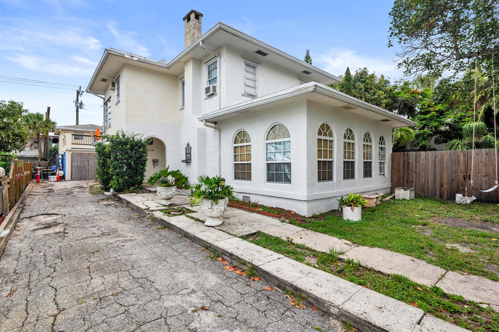 A two-story white stucco house features a sunroom with arched windows and a cracked driveway — 821 Omar Road, West Palm Beach FL 33405, WEST PALM BEACH, FL