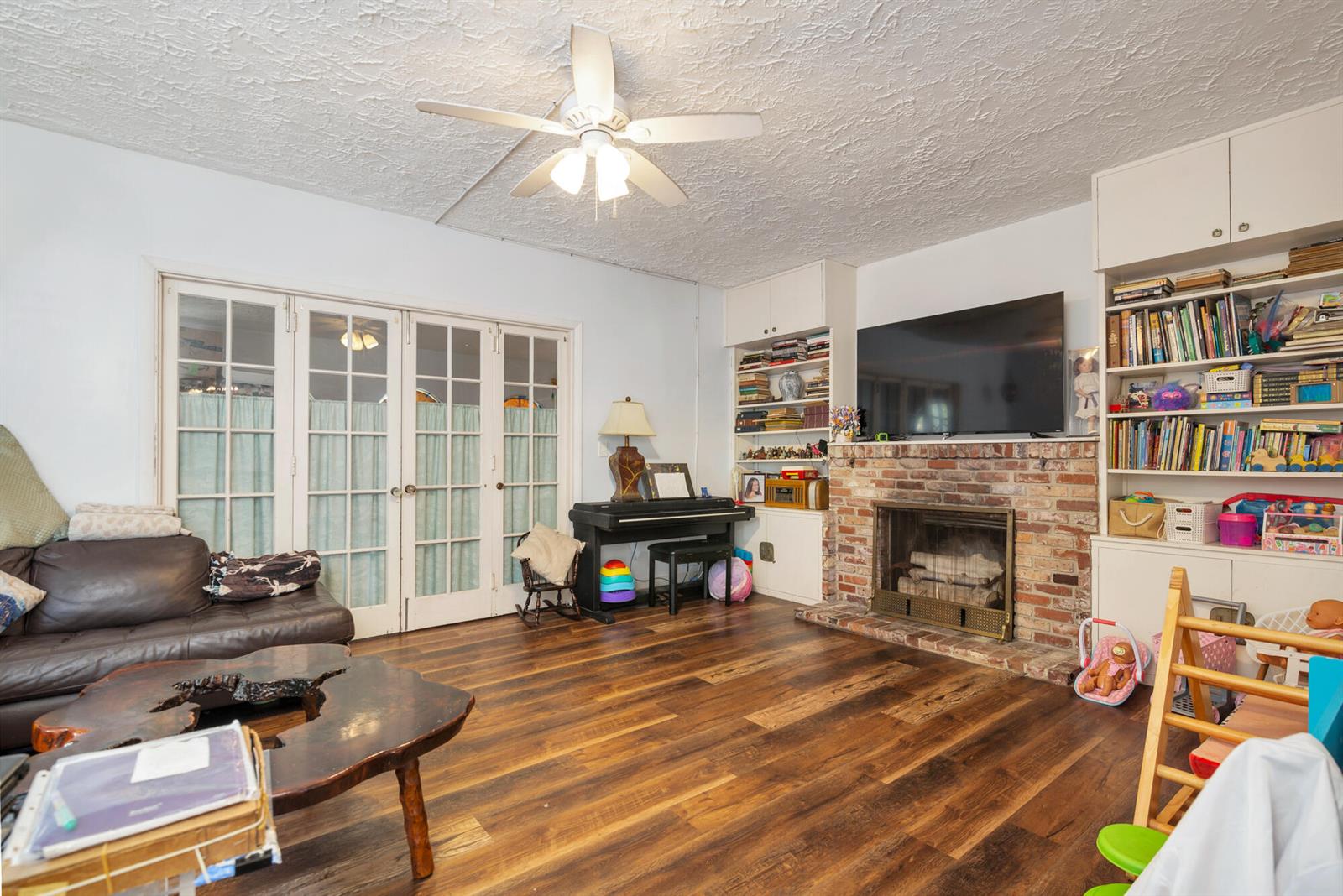A living room features a brick fireplace, built-in shelving, wood flooring, and a ceiling fan — 821 Omar Road, West Palm Beach FL 33405, WEST PALM BEACH, FL