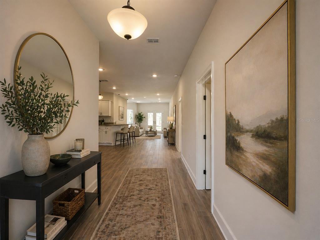 A hallway with wood-look flooring leads to an open-concept kitchen and living area — 12992 KENT BRADLEY STREET, DADE CITY, FL