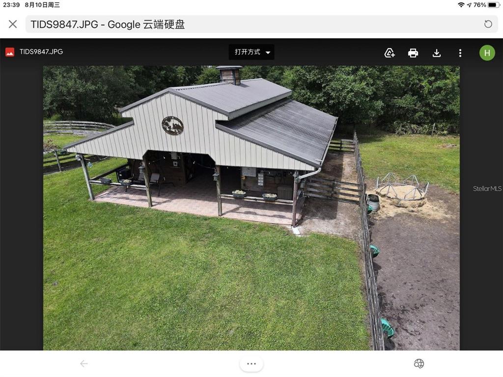 An aerial view of a metal-roofed barn with an open-air porch and adjacent fenced pasture — 3060 RAMBLER AVENUE, ST CLOUD, FL