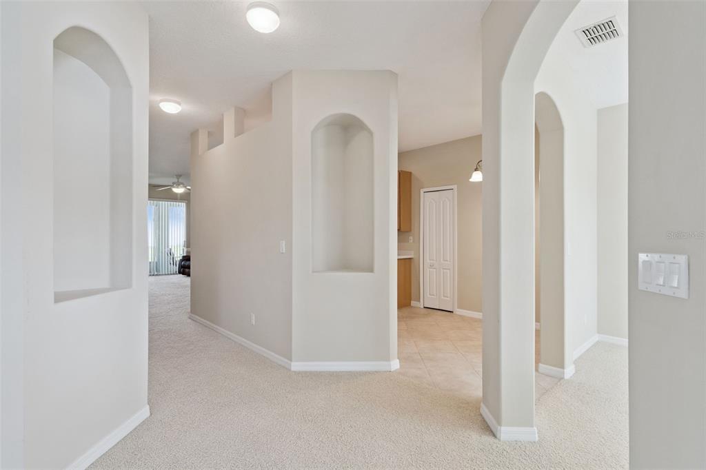 An interior hallway features arched wall niches, beige carpeting, and tile flooring leading to a kitchen — 2925 DAYTON DRIVE, WINTER HAVEN, FL