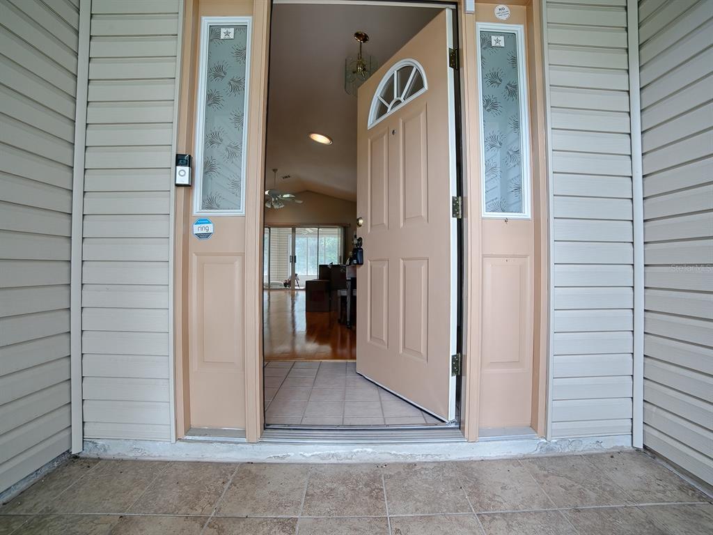 A beige front door stands open, revealing an interior living space with hardwood floors — 419 RANCHWOOD DRIVE, LEESBURG, FL