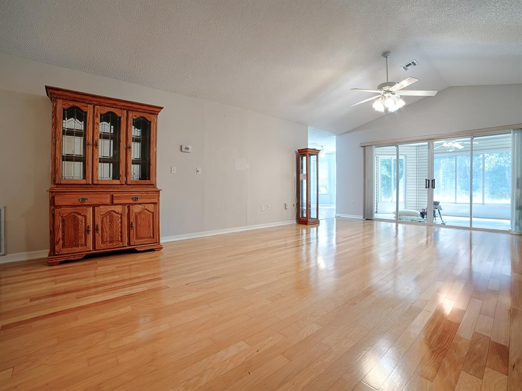 A spacious living room features light hardwood floors, a large wooden hutch, and sliding glass doors — 419 RANCHWOOD DRIVE, LEESBURG, FL