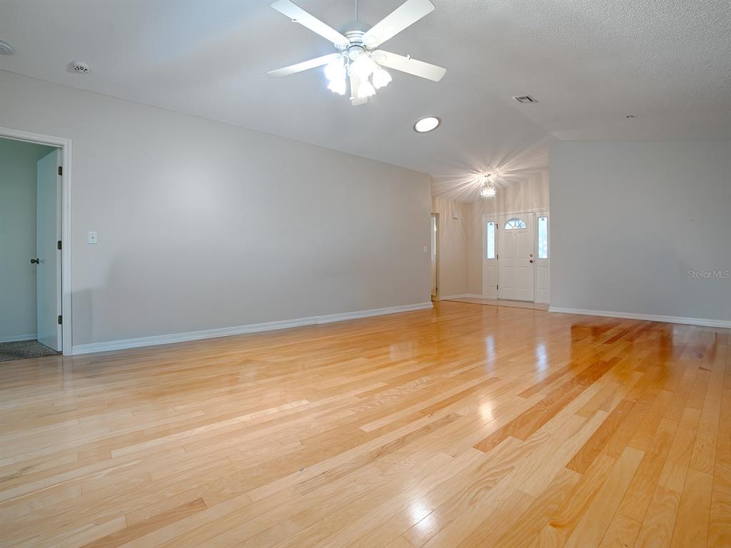 A spacious living room features light-colored walls, hardwood flooring, and a ceiling fan — 419 RANCHWOOD DRIVE, LEESBURG, FL