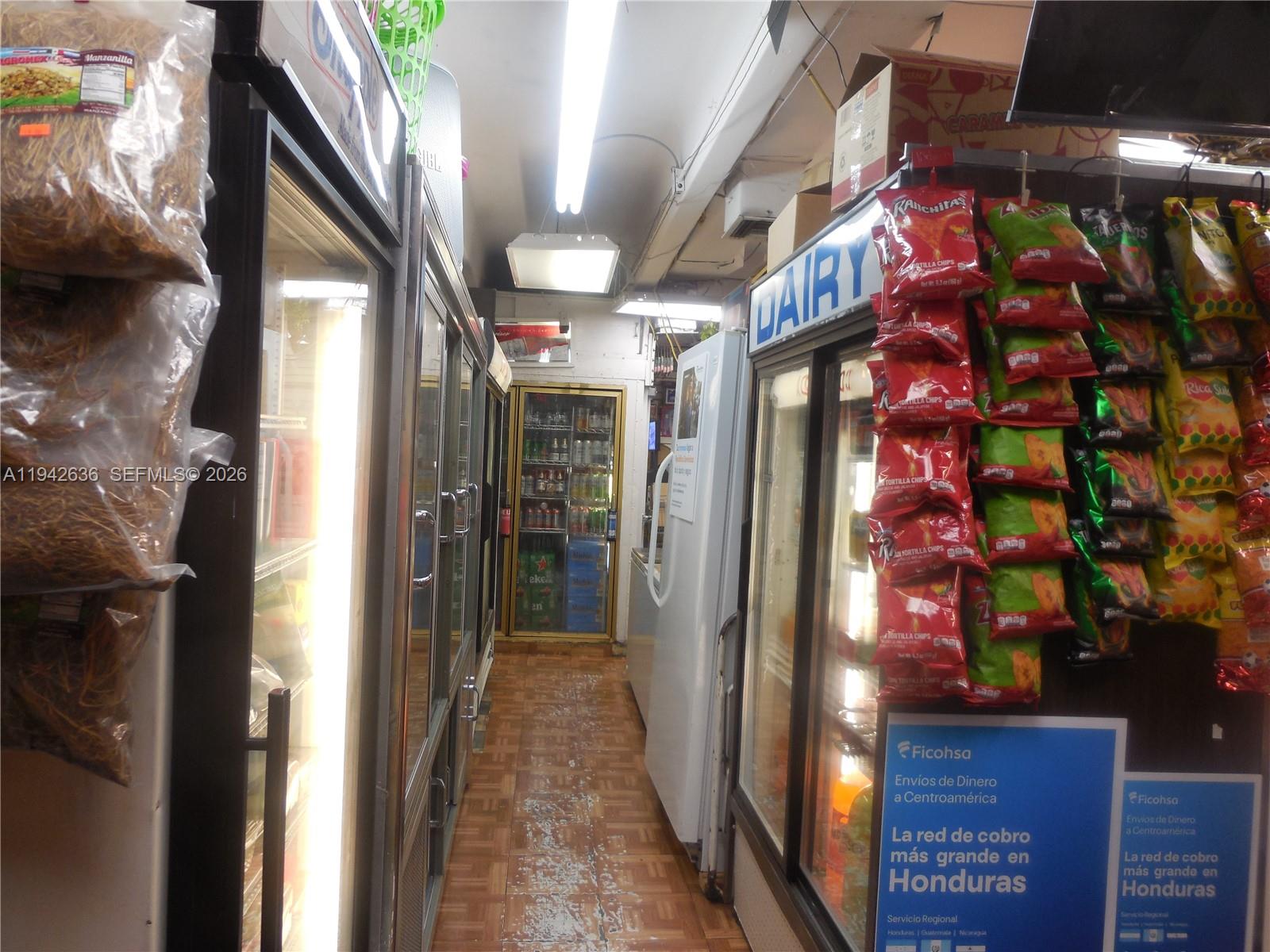 A narrow aisle in a convenience store features refrigerated display cases and hanging snack bags — NW 12th Ave, Miami FL 33128, MIAMI, FL