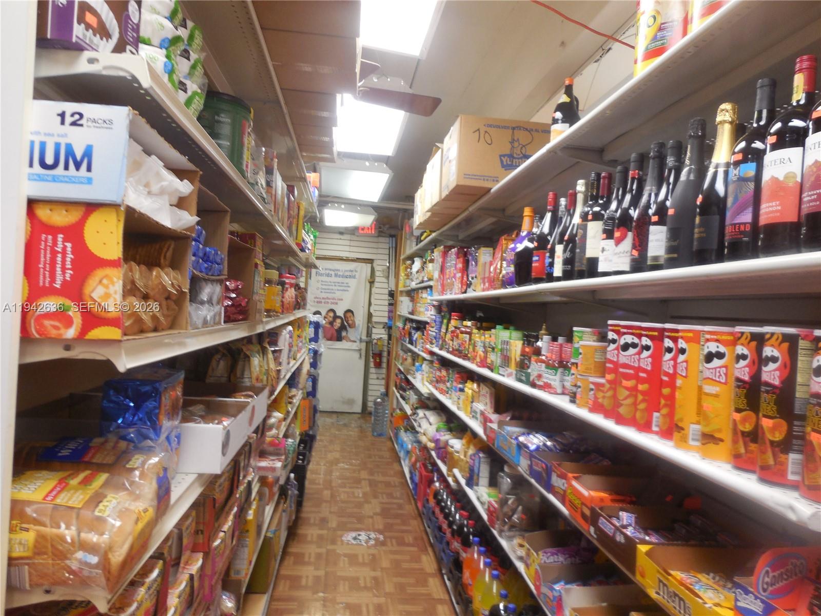A narrow grocery store aisle is lined with shelves stocked with various food and beverage products — NW 12th Ave, Miami FL 33128, MIAMI, FL