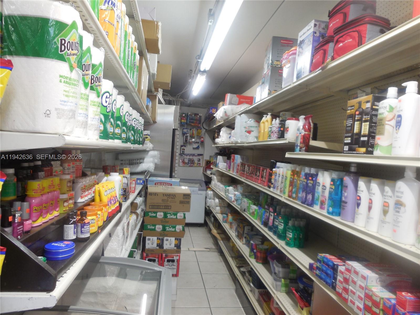 A narrow aisle in a retail store is lined with shelves stocked with various household products — NW 12th Ave, Miami FL 33128, MIAMI, FL