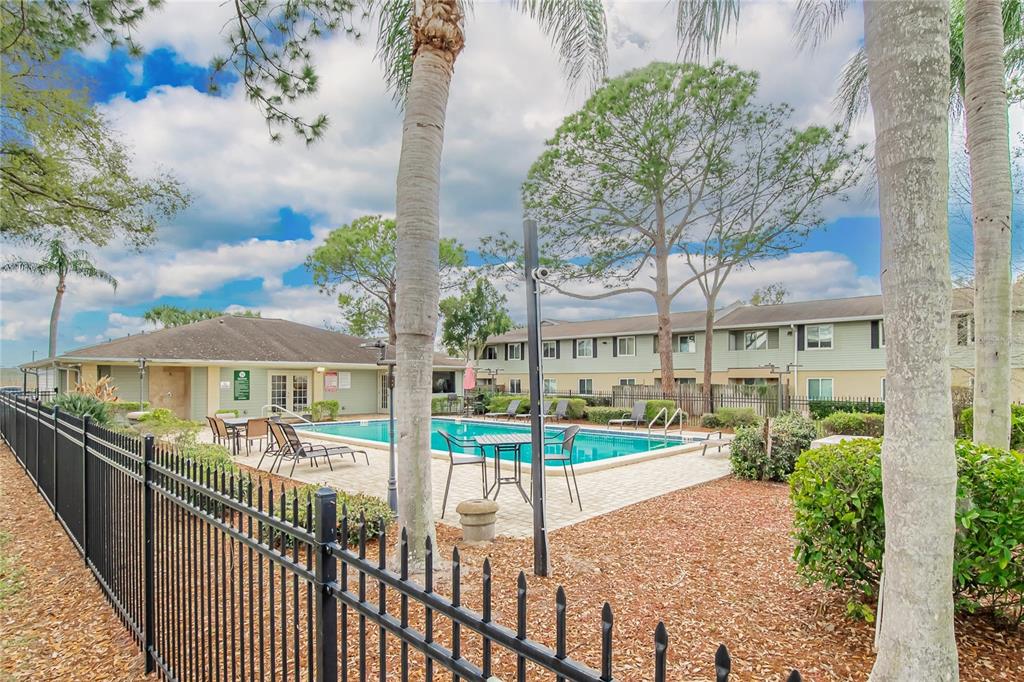 A swimming pool with lounge chairs and tables is surrounded by a fence and trees — 202 RED MAPLE PLACE UNIT 202, BRANDON, FL