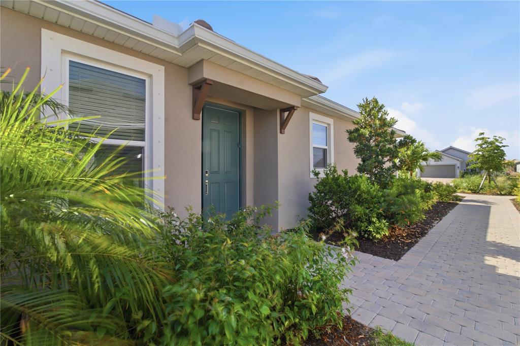 A teal front door is centered on the tan exterior of a single-story house — 16255 SAN DONATO PLACE, BRADENTON, FL