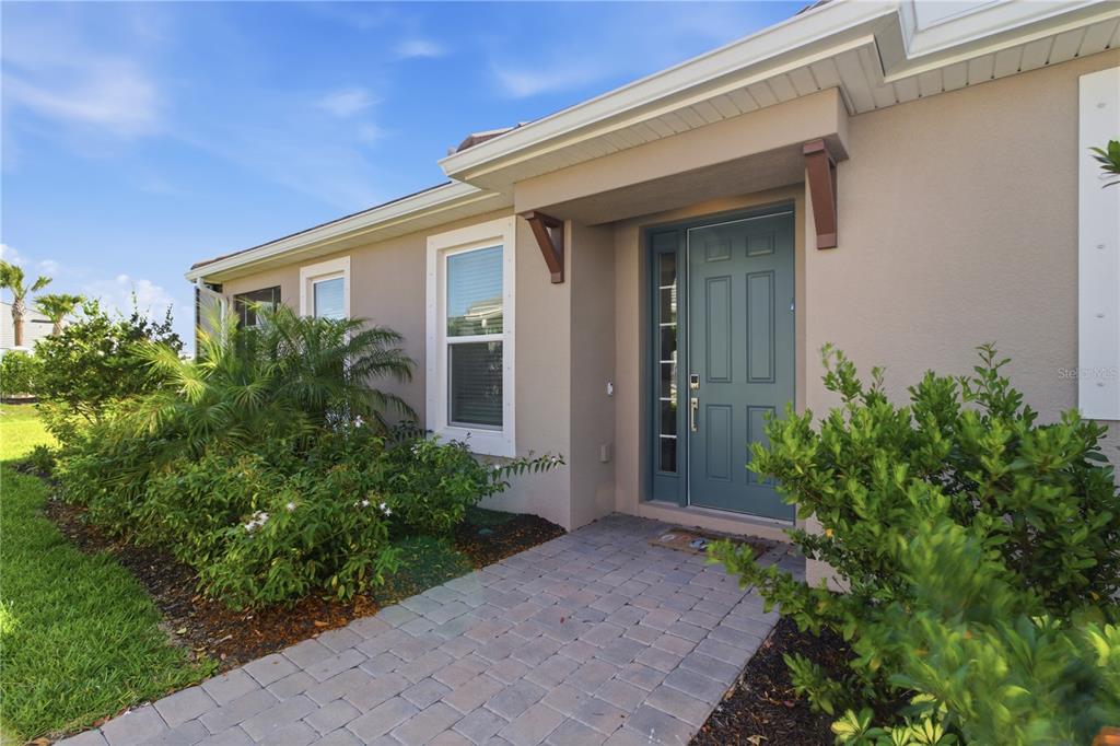 A paved walkway leads to the front entrance of a house with a blue door — 16255 SAN DONATO PLACE, BRADENTON, FL