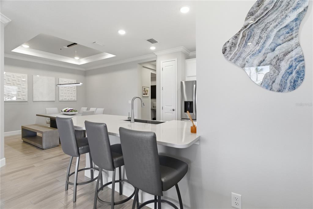 A kitchen island with bar stools overlooks a dining area with a tray ceiling — 16255 SAN DONATO PLACE, BRADENTON, FL