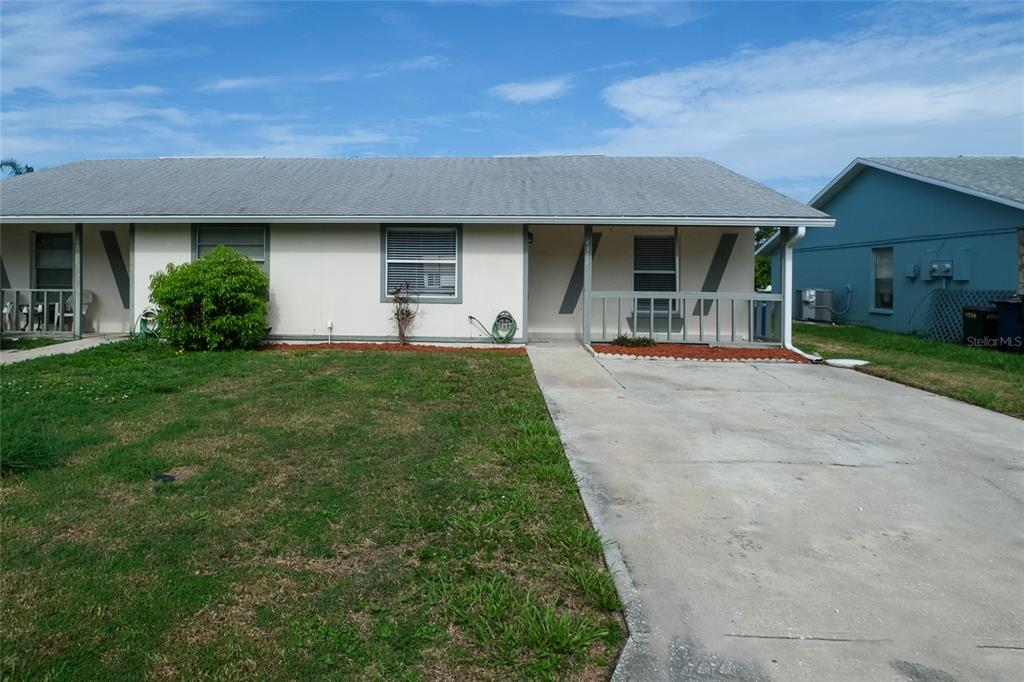 A single-story duplex with a concrete driveway, a small front lawn, and a covered porch — 4304 78TH STREET W UNIT 54, BRADENTON, FL