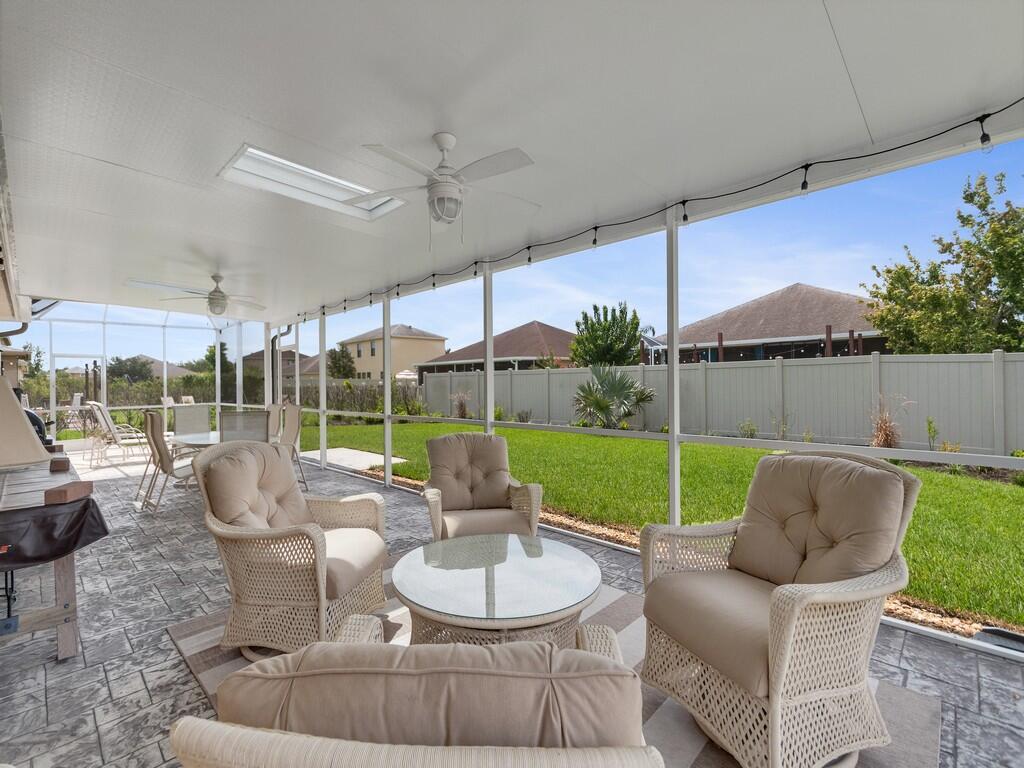 A screened-in patio features wicker furniture, a glass-top table, and a view of the backyard — 10105 Verona Manor, Vero Beach FL 32966, VERO BEACH, FL