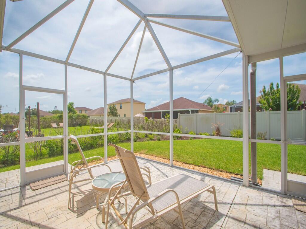 A screened-in patio with a tiled floor, two lounge chairs, and a view of a backyard — 10105 Verona Manor, Vero Beach FL 32966, VERO BEACH, FL