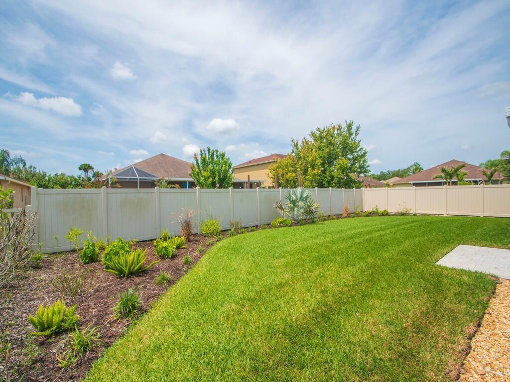 A backyard features a green lawn, a garden bed with small plants, and a vinyl fence — 10105 Verona Manor, Vero Beach FL 32966, VERO BEACH, FL