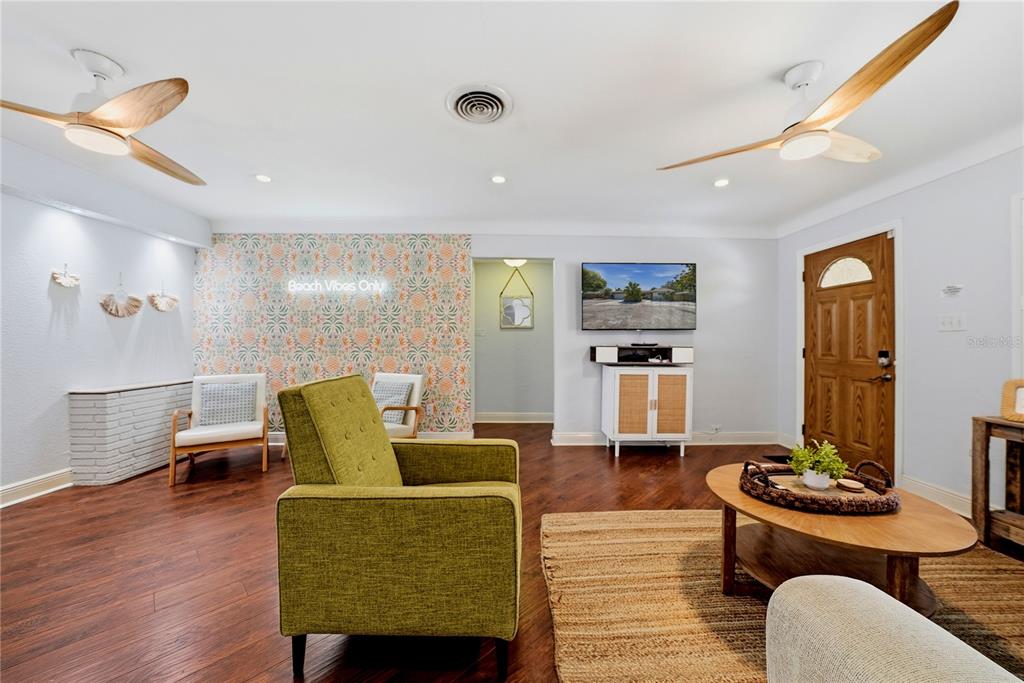 A living room features a green armchair, patterned wallpaper, two ceiling fans, and wood flooring — 955 INDIAN ROCKS ROAD S, LARGO, FL