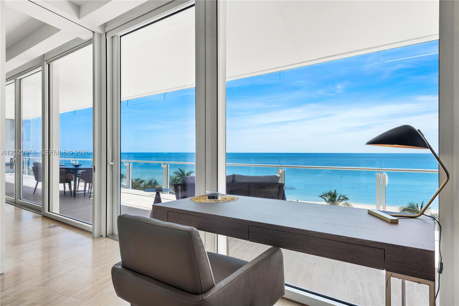 A modern office space features a desk and chair overlooking a balcony and the ocean — 9001 Collins Ave # 509, Surfside FL 33154, SURFSIDE, FL