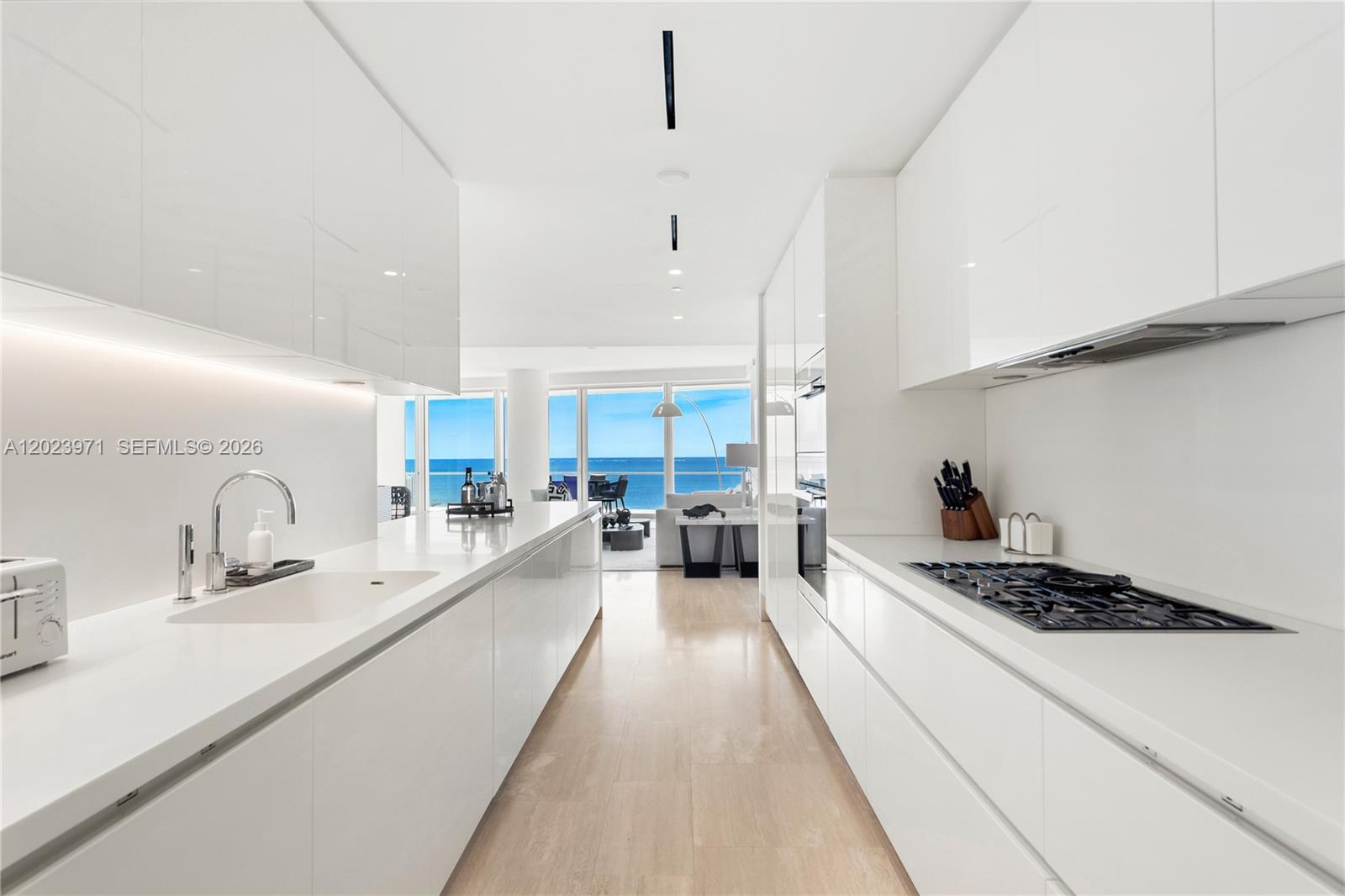 A modern white galley kitchen features sleek cabinetry, integrated appliances, and a view of the ocean — 9001 Collins Ave # 509, Surfside FL 33154, SURFSIDE, FL