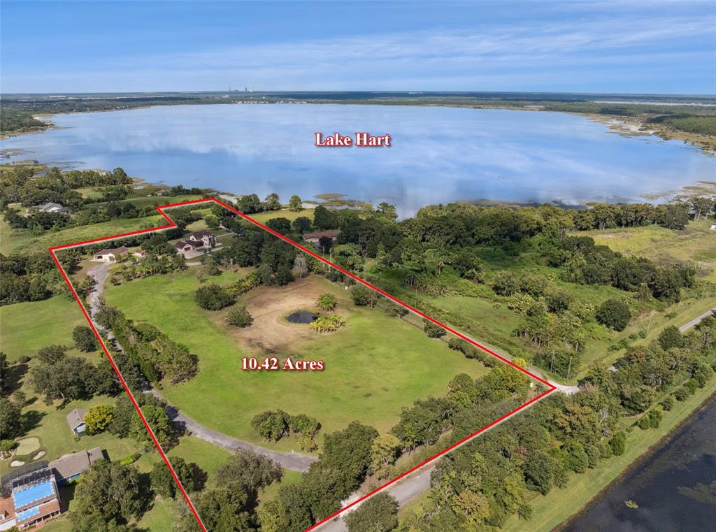 An aerial view shows a large grassy lot with a pond and houses near Lake Hart — 11205 TINDALL ROAD, ORLANDO, FL