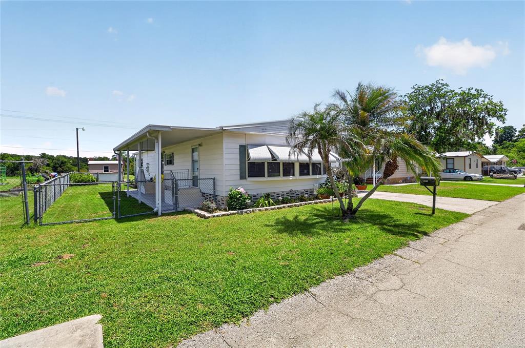 A single-story mobile home with a covered porch, chain-link fence, and a palm tree — 3586 LAZY LAKE DRIVE N, LAKELAND, FL