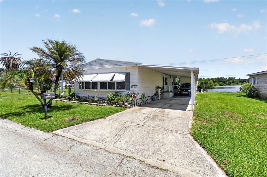 A single-story manufactured home with a concrete driveway, carport, and palm trees on a lawn — 3586 LAZY LAKE DRIVE N, LAKELAND, FL