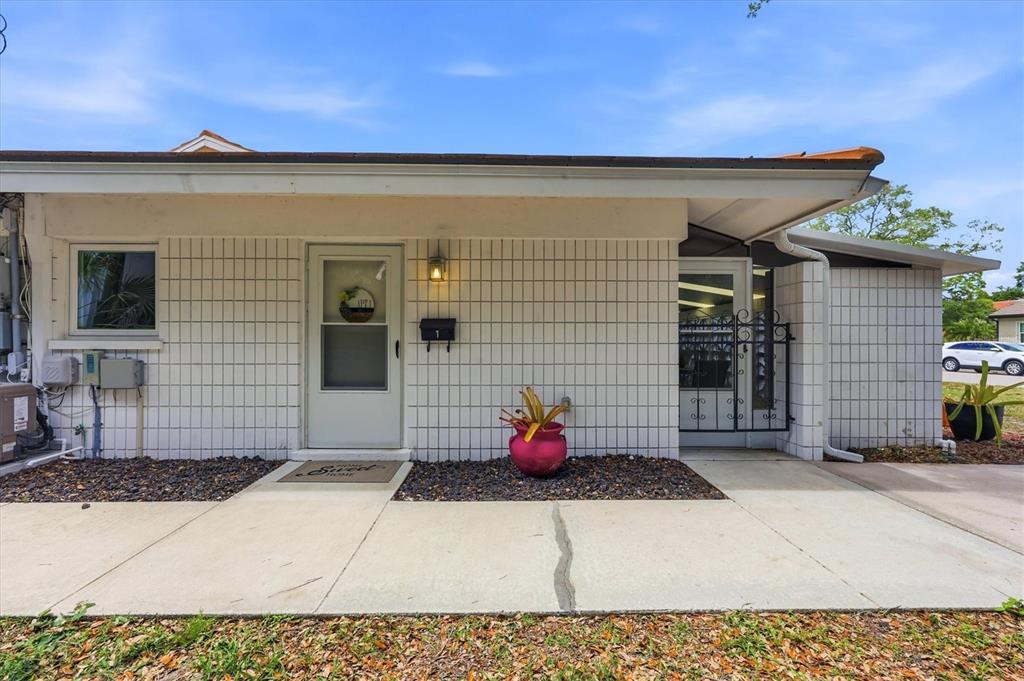 The exterior of a single-story building features white tiled walls, a front door, and a walkway — 405 MENENDEZ STREET, VENICE, FL