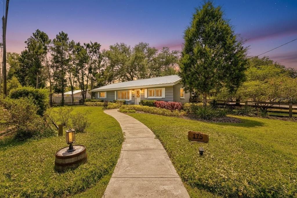 A single-story house with a metal roof and a curved concrete walkway in the yard — 175 RIVIERE ROAD, PALM HARBOR, FL