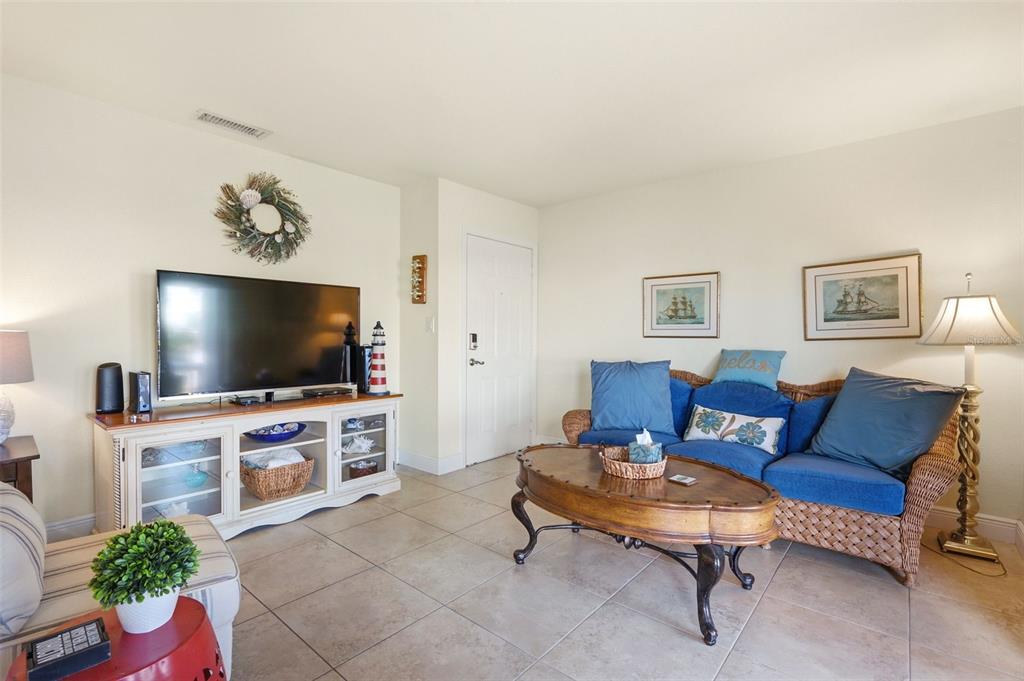 A living room features tile flooring, a wicker sofa, a television console, and coastal decor — 5191 SALMON DRIVE SE UNIT B, ST PETERSBURG, FL