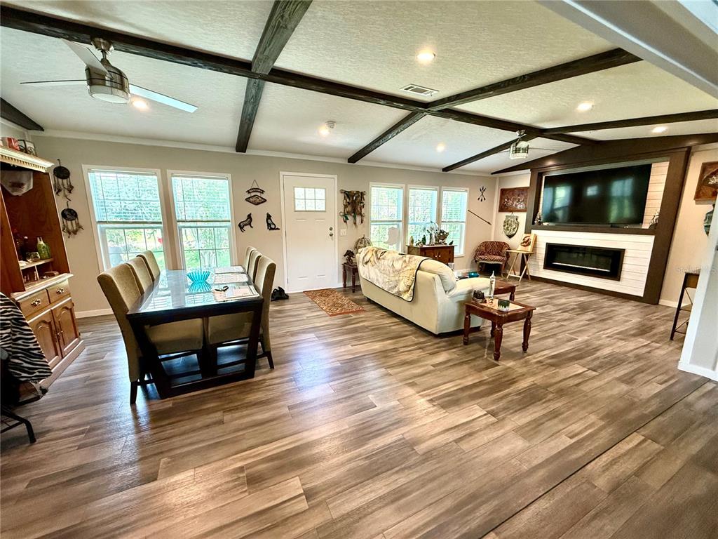 An open-concept living and dining area features wood-look flooring and dark ceiling beams — 7589 CR 763, BUSHNELL, FL