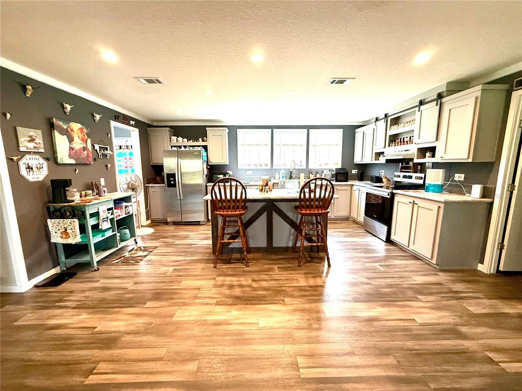 A kitchen features wood-look flooring, a central island with two chairs, and white cabinetry — 7589 CR 763, BUSHNELL, FL