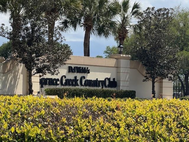 The entrance sign for Spruce Creek Country Club stands behind a hedge of yellow flowers — 14031 DEL WEBB BOULEVARD UNIT 100, SUMMERFIELD, FL