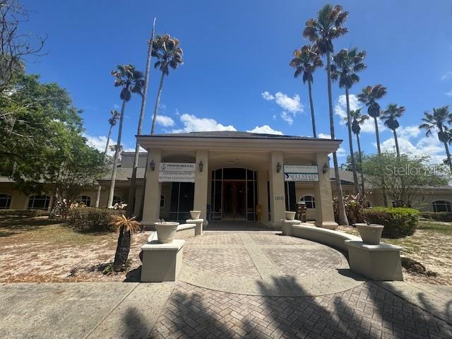 A low-rise commercial building with a paved entrance and palm trees under a blue sky — 14031 DEL WEBB BOULEVARD UNIT 100, SUMMERFIELD, FL