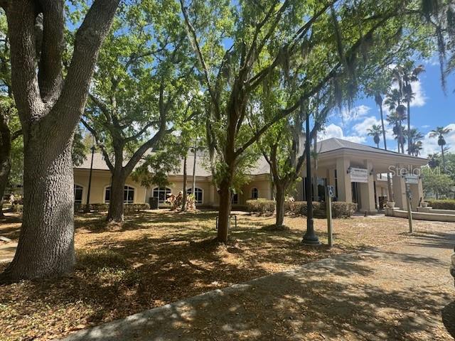 A tan, single-story commercial building with a covered entrance is surrounded by large, mature trees — 14031 DEL WEBB BOULEVARD UNIT 100, SUMMERFIELD, FL