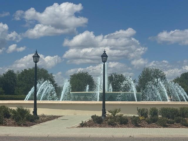 A large outdoor fountain sits behind two black lampposts on a paved walkway — 14031 DEL WEBB BOULEVARD UNIT 100, SUMMERFIELD, FL