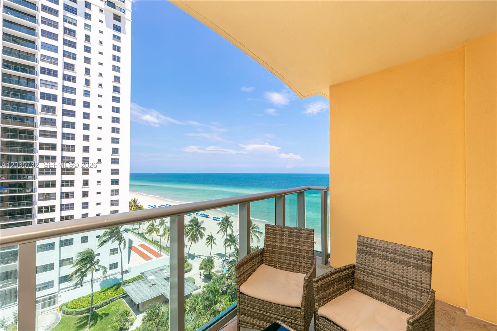 A balcony with two wicker chairs overlooks the ocean and a neighboring high-rise building — 2501 S Ocean Dr # 1008, Hollywood FL 33019, HOLLYWOOD, FL