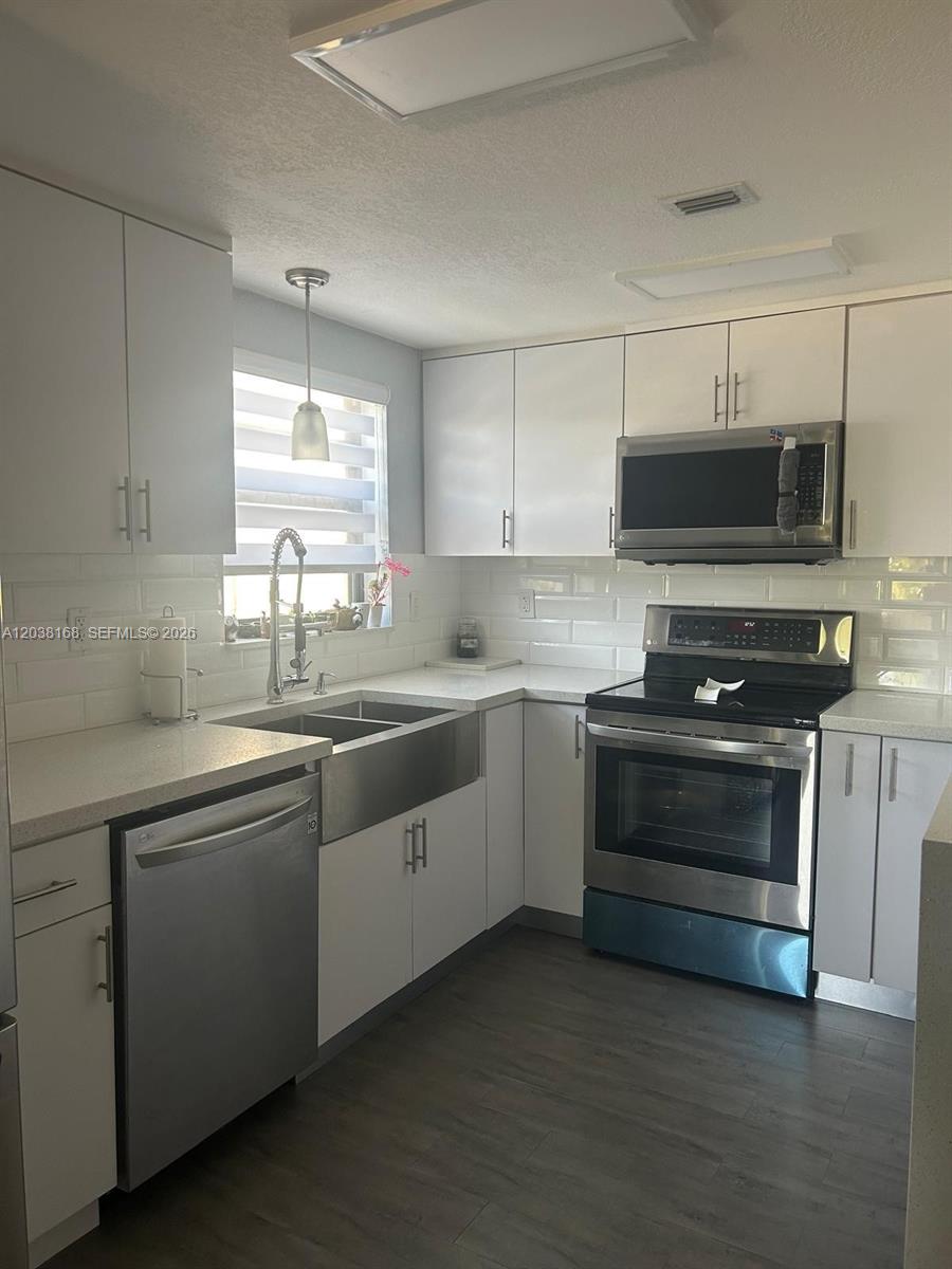 A kitchen features white cabinets, stainless steel appliances, a farmhouse sink, and subway tile backsplash — 8820 SW 123rd Ct # L410, Miami FL 33186, MIAMI, FL