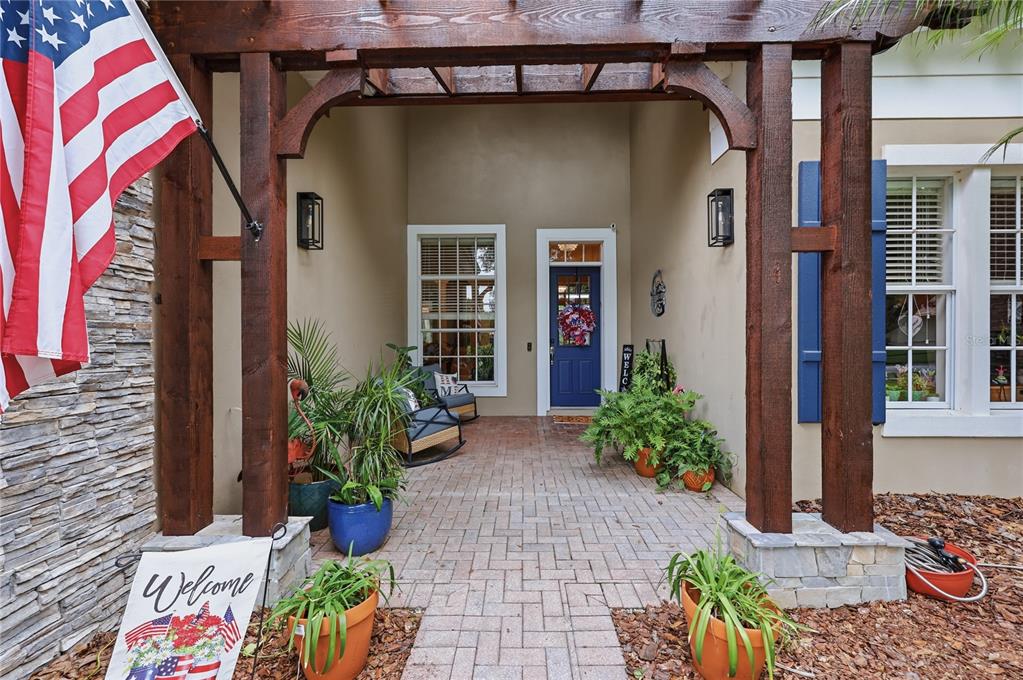 A covered brick entryway features a blue front door, rocking chairs, and potted plants — 7049 TIMBER RIDGE WAY, LAND O LAKES, FL