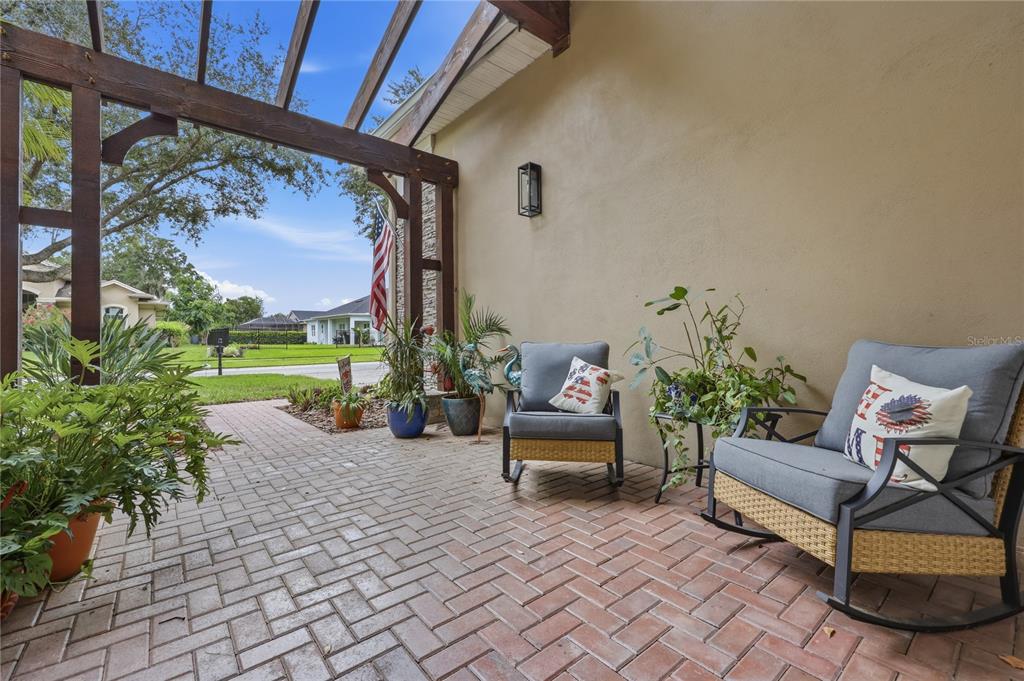 A brick patio features a wooden pergola, two rocking chairs, and potted plants — 7049 TIMBER RIDGE WAY, LAND O LAKES, FL