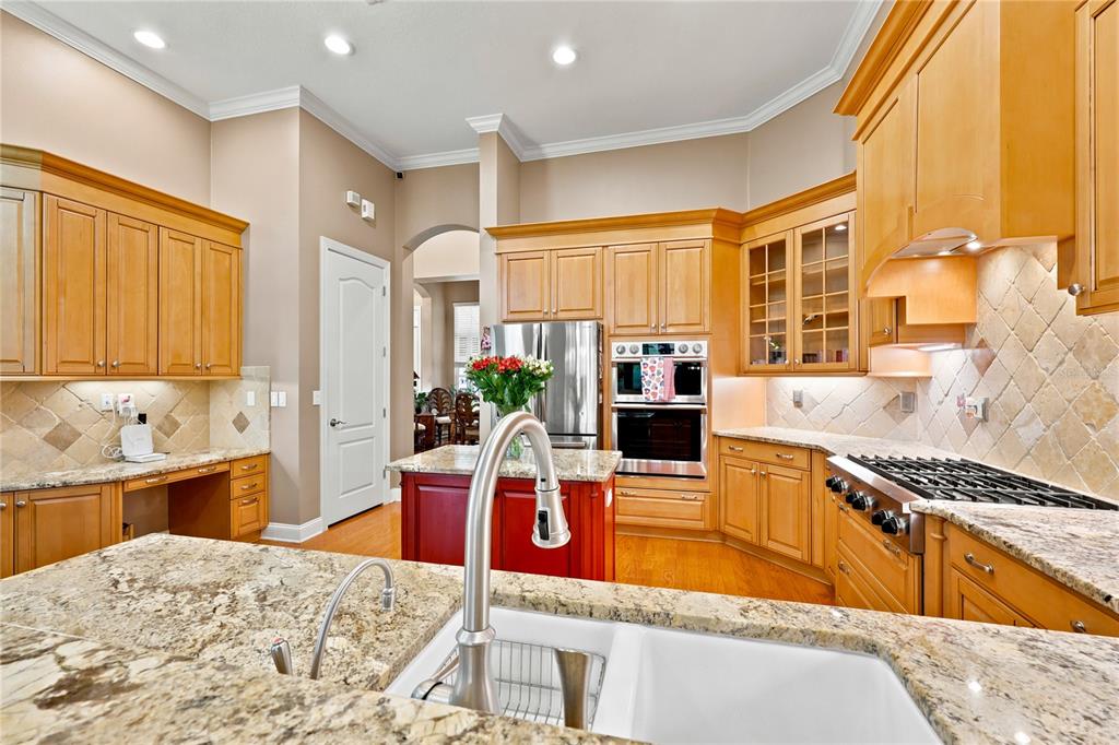 A kitchen features light wood cabinets, granite countertops, a red island, and stainless steel appliances — 7049 TIMBER RIDGE WAY, LAND O LAKES, FL