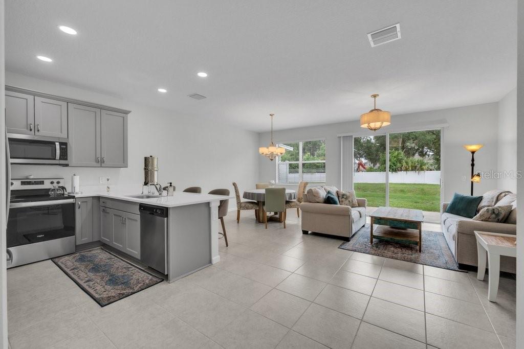 An open-concept kitchen, dining area, and living room with light tile flooring and sliding doors — 10967 QUICKWATER COURT, RIVERVIEW, FL