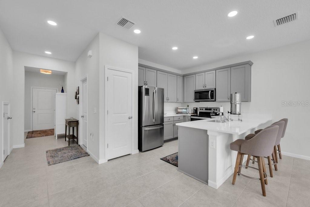 A modern kitchen features gray cabinets, stainless steel appliances, and a white island with stools — 10967 QUICKWATER COURT, RIVERVIEW, FL