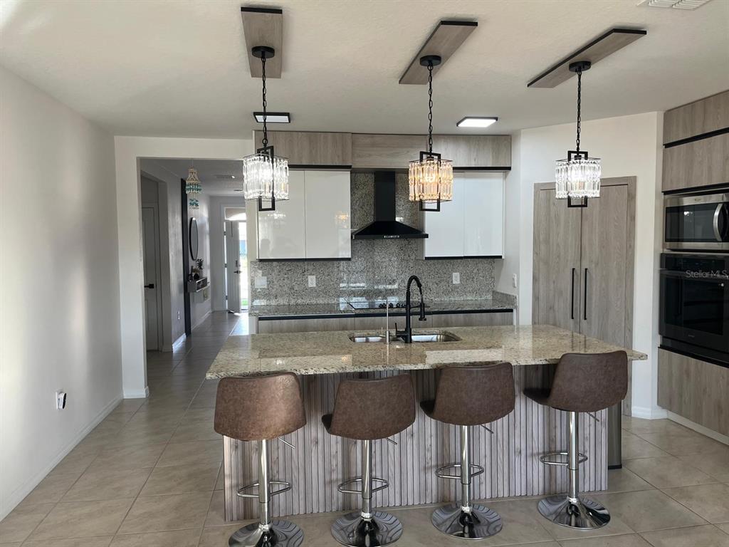 A modern kitchen features a granite island with four bar stools and wood-toned cabinetry — 1538 BITTEROOT STREET, KISSIMMEE, FL