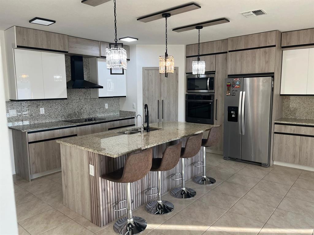 A modern kitchen features a granite-topped island with bar stools, wood-toned cabinetry, and stainless appliances — 1538 BITTEROOT STREET, KISSIMMEE, FL