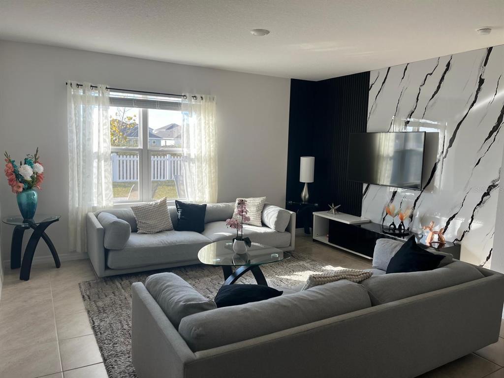 A living room features a marble-patterned accent wall, black slat paneling, and two gray sofas — 1538 BITTEROOT STREET, KISSIMMEE, FL