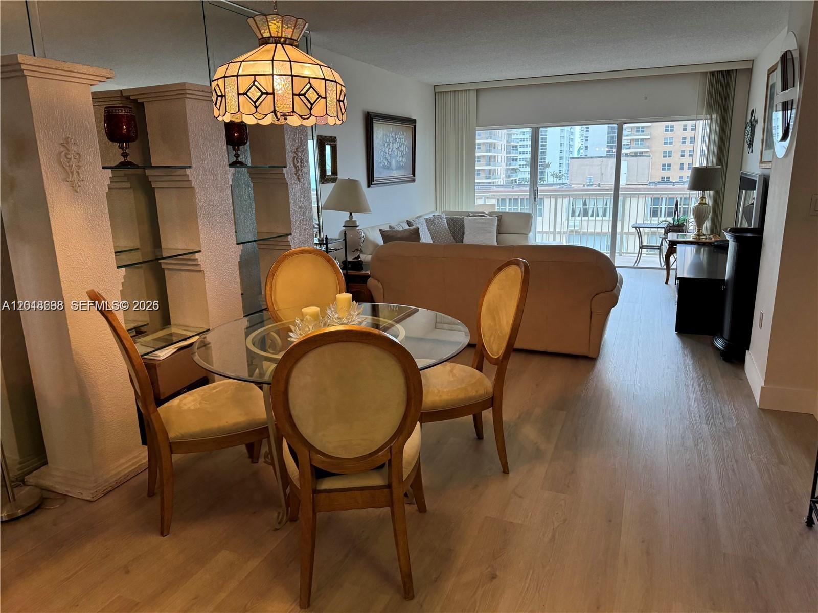 A dining area with a glass table and chairs sits before a living room balcony — 1950 S Ocean Dr # 4D, Hallandale Beach FL 33009, HALLANDALE BEACH, FL
