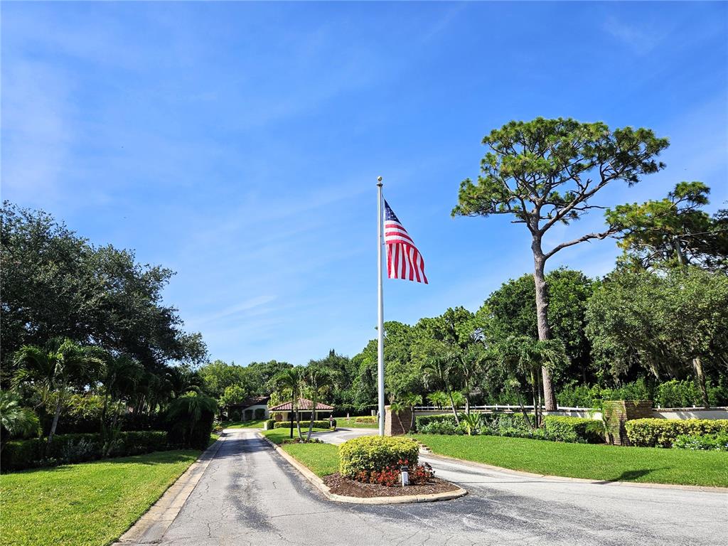 A paved driveway leads toward a gated entrance featuring an American flag and landscaping — 1800 MARINER DRIVE UNIT 9, TARPON SPRINGS, FL