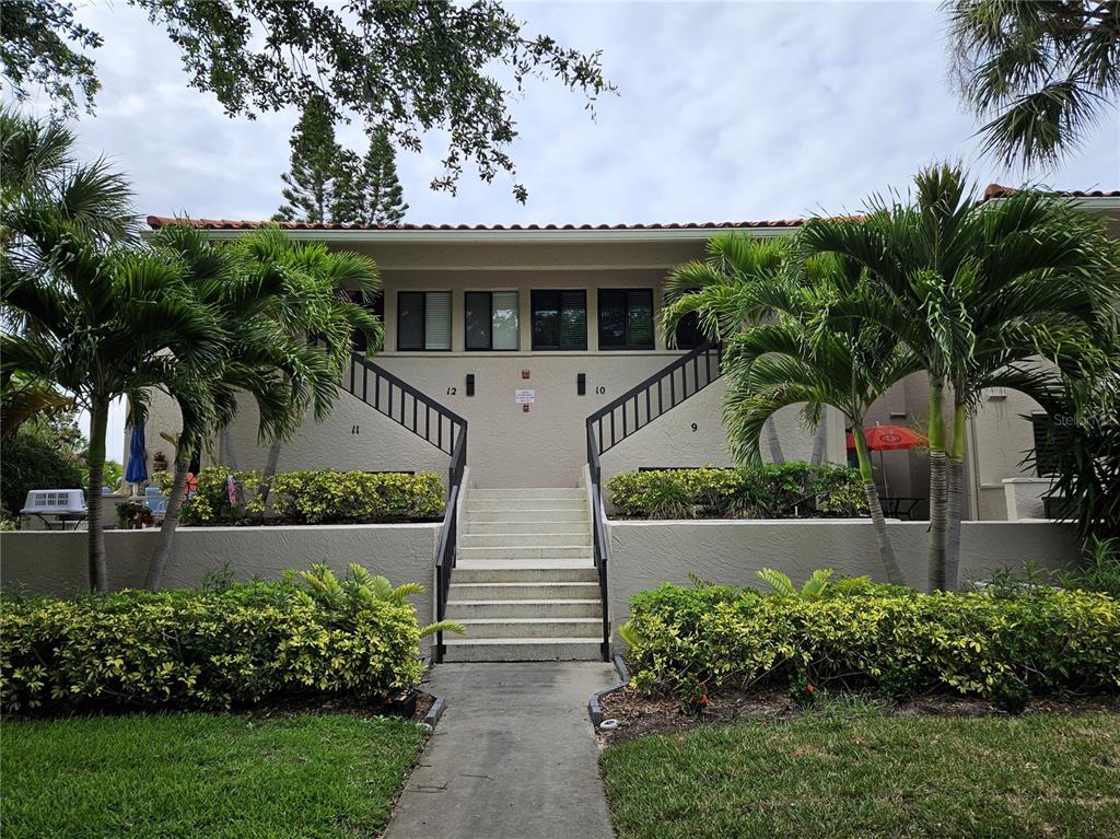 A two-story apartment building exterior features a central staircase, palm trees, and landscaped bushes — 1800 MARINER DRIVE UNIT 9, TARPON SPRINGS, FL